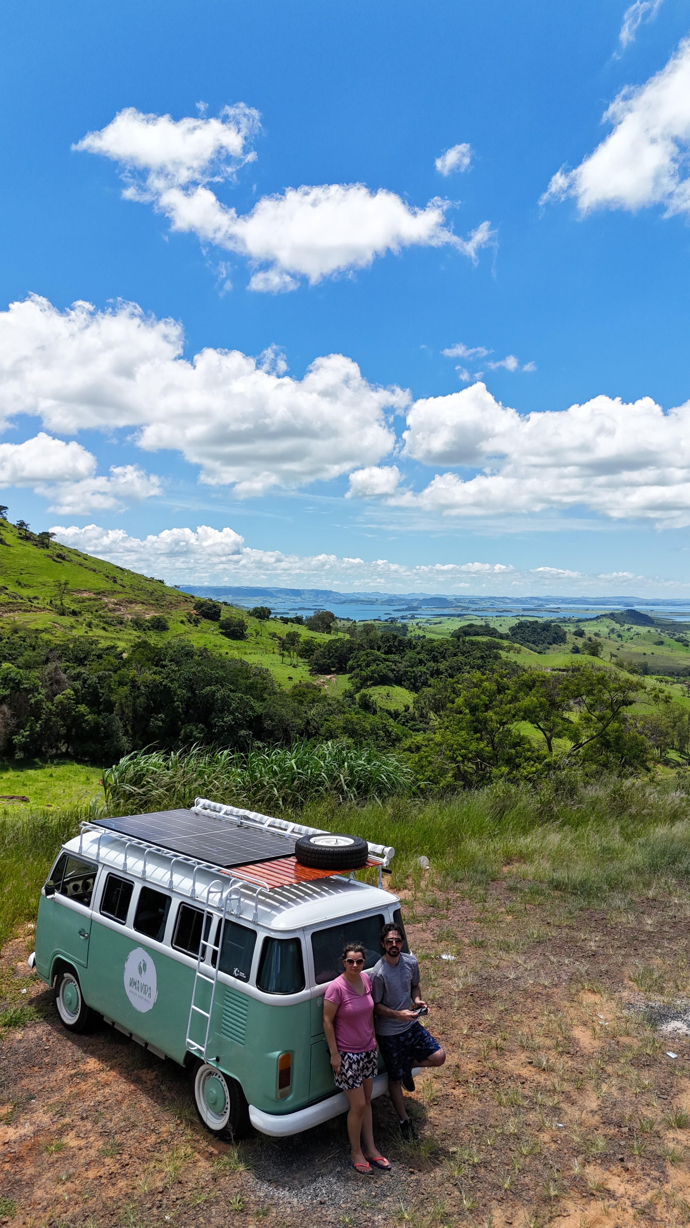 Casal sorrindo ao lado da kombi em uma estrada de terra